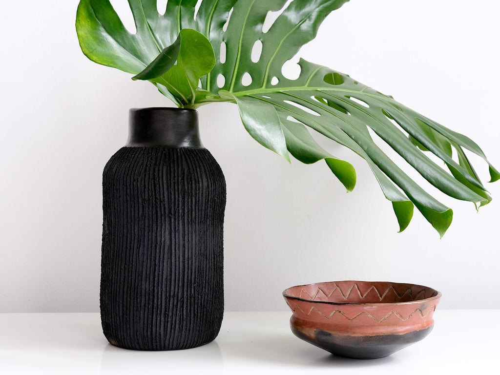 Black textured vase with a plant and a terracotta bowl on a white surface